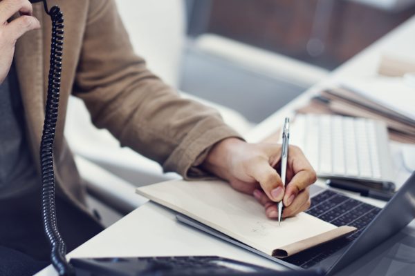 Closeup of hand writing note while on the phone